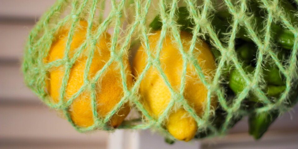 Frische gelbe Zitronen und grüne Paprika in einem Lebensmittel-Mesh-Netz-Beutel